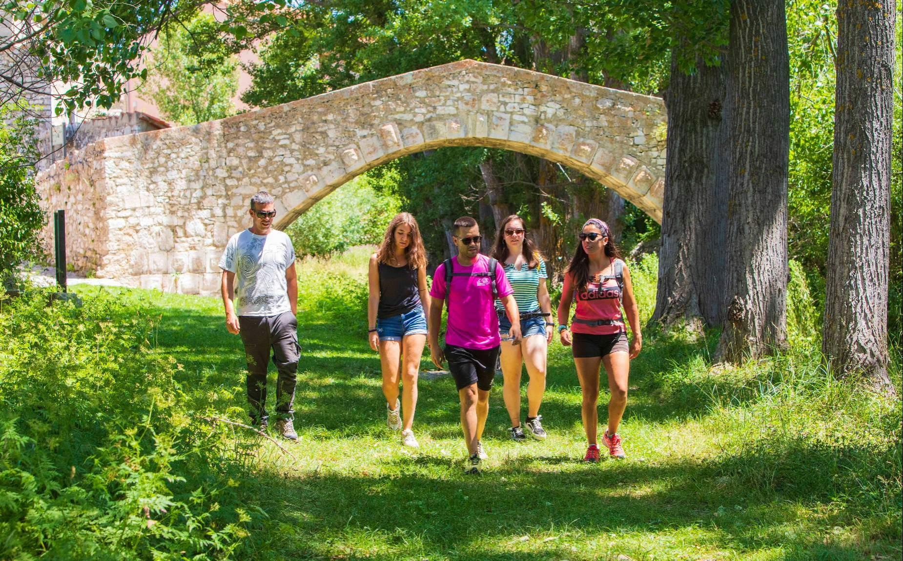 Varias personas paseando por la naturaleza con un puente de piedra a sus espaldas
